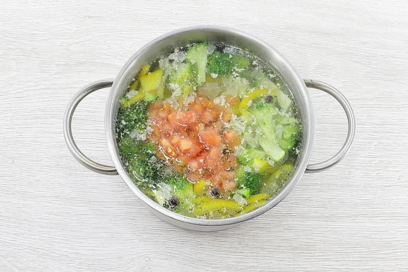 Добавить нарезанный помидор, перемешать и довести до кипения. Варить 5–7 минут на слабом огне до полной готовности овощей.