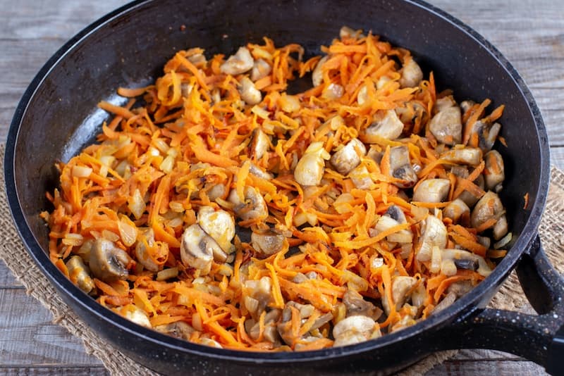 На сухой сковороде обжарить грибы, порезанные четвертинками. Затем добавить к ним растительное масло, морковь, лук.