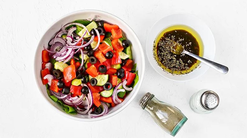 Оливки для салата разрежьте на половинки. Добавьте в миску к помидорам вместе со всеми остальными овощами и петрушкой. Для заправки оливковое масло взбейте вилкой с уксусом, орегано, солью и перцем.