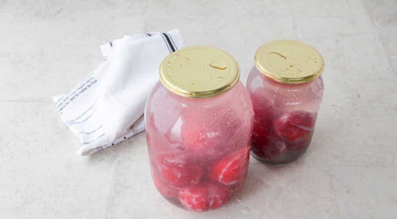 Залейте сливы кипящим сиропом и снова накройте банки крышками. Оставьте на 5 мин. В это время компот начнет менять цвет – жидкость будет окрашиваться сливами.