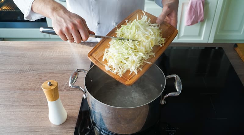В кастрюлю, в которой будут вариться постные щи, влейте воду. На сильном огне доведите ее до кипения и немного посолите. Капусту тонко нашинкуйте и выложите в кастрюлю. Варите 7 минут.