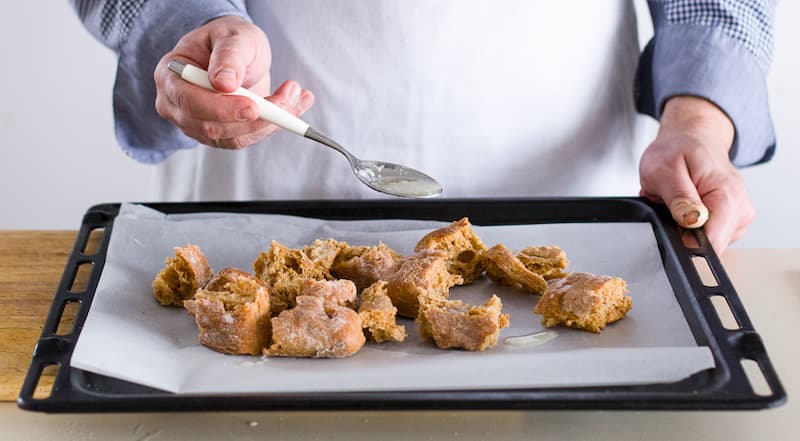 Нарвите чиабатту руками на удобные для еды кусочки. Застелите противень бумагой¬ для выпечки, сбрызните чесночным маслом (примерно половину оставьте) и поставьте противень в духовку. Запекайте, пока хлеб не подрумянится. Остудите гренки для постного салат