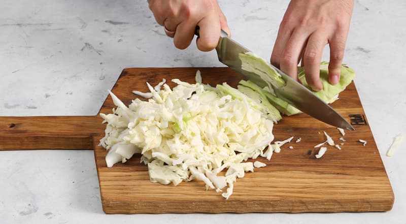 Кочан белокочанной капусты очистите от верхних листьев. Разрежьте пополам или на четыре части и удалите кочерыжку. Капусту нарежьте тонкими полосками или маленькими кубиками.