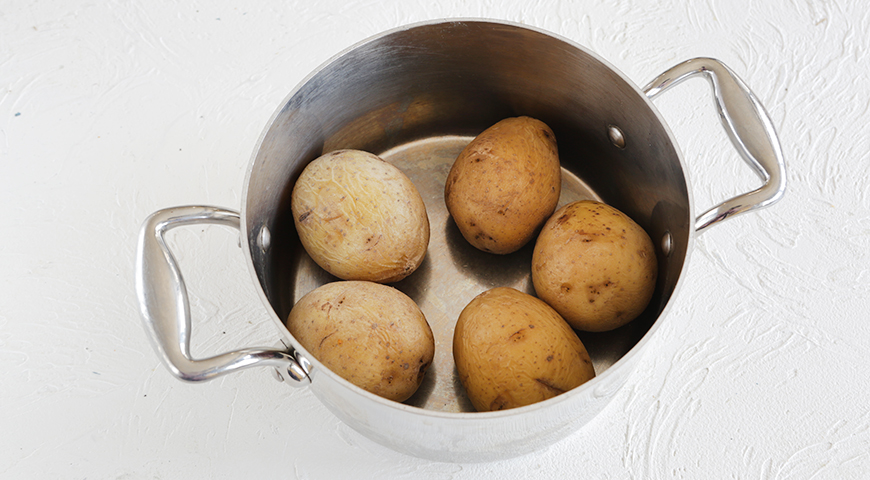 Подготовьте ингредиенты для окрошки. Картофель вымойте с помощью щетки и сложите в кастрюлю. Залейте горячей водой и доведите до кипения. Варите 30 минут. Дайте полностью остыть.