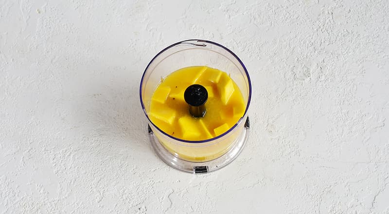 Для фруктового слоя очистите манго и срежьте мякоть с косточки. Примерно четверть отложите для украшения. Оставшееся манго сложите в блендер. Добавьте 500 мл апельсинового сока и измельчите.