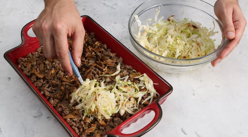 Форму для запеканки смажьте оставшимся маслом и выложите в нее слоями половину капусты, фарш, белые грибы и оставшуюся капусту. Для соуса яйца взбейте со сметаной. Добавьте сыр, посолите, поперчите и перемешайте. Соусом залейте содержимое формы. Готовьте 