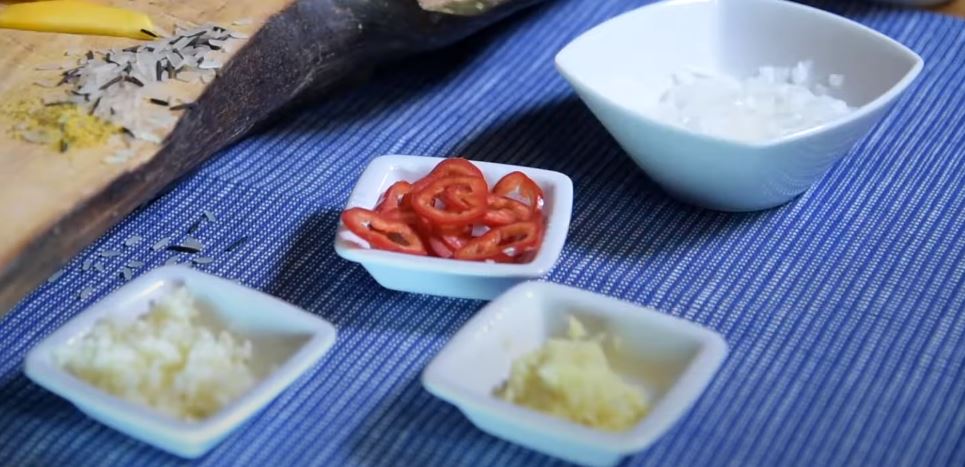 Подготовить все ингредиенты для карри: лук нарезать мелкими кубиками, перец чили очистить от косточек и нарезать кольцами. Корень имбиря и чеснок натереть на мелкой тёрке до получения пюре. Рыбу нарезать крупными кубиками.