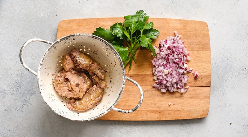 Откройте банку с печенью трески и выложите кусочки на мелкое сито, чтобы стекло масло. Красную луковицу очистите и очень мелко нарежьте. Петрушку вымойте и хорошо обсушите. Оборвите с веточки листочки.