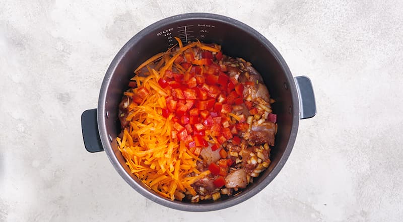 Гречку переберите и промойте проточной водой. Курицу в маринаде переложите в чашу мультиварки. Добавьте морковь и сладкий перец, разровняйте. Сверху распределите гречку. Снова разровняйте.