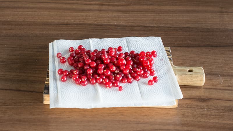 Подготовьте красную смородину для желе. Отделите ягоды от веточек и переберите. Тщательно промойте проточной водой и хорошо обсушите, разложив на бумажных полотенцах.