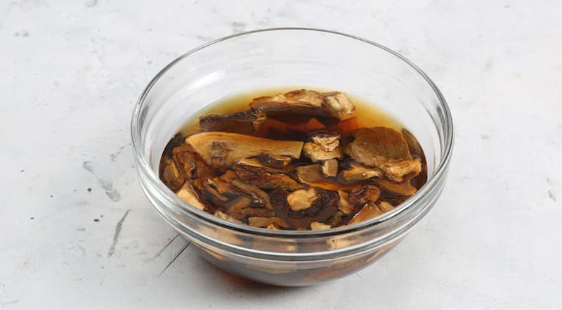 Подготовьте ингредиенты для капустной запеканки в духовке. Сухие грибы поместите в небольшую мисочку, залейте горячей питьевой водой (250 мл) и оставьте в теплом месте на 30 минут.