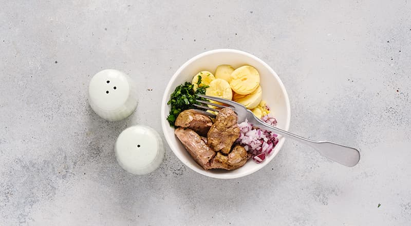 Яйца очистите от скорлупы и разрежьте вдоль на половинки. Выньте желтки. Разомните вилкой, перемешайте с печенью трески и нарезанным красным луком. Немного поперчите.