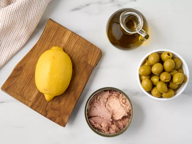 Откройте банки с тунцом и оливками, слейте жидкость. Помойте лимон, вытрите его полотенцем. Поставьте на стол блендер с чашей, достаньте салатник.