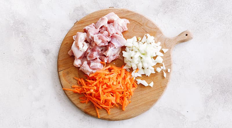 Подготовьте все ингредиенты. Курицу вымойте и нарежьте кубиками. Переложите в большую миску. Лук и чеснок очистите, мелко нарежьте. Морковь очистите, вымойте и натрите на крупной терке. Сладкий перец, удалив семена, нарежьте мелкими кубиками.