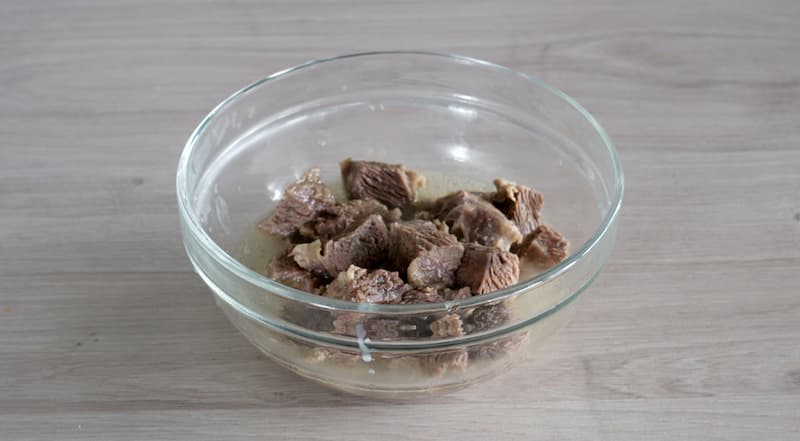 Бульон для харчо процедите через частое сито. Мякоть говядины отделите от кости, нарежьте и сложите в небольшую емкость. Залейте половником бульона и закройте.