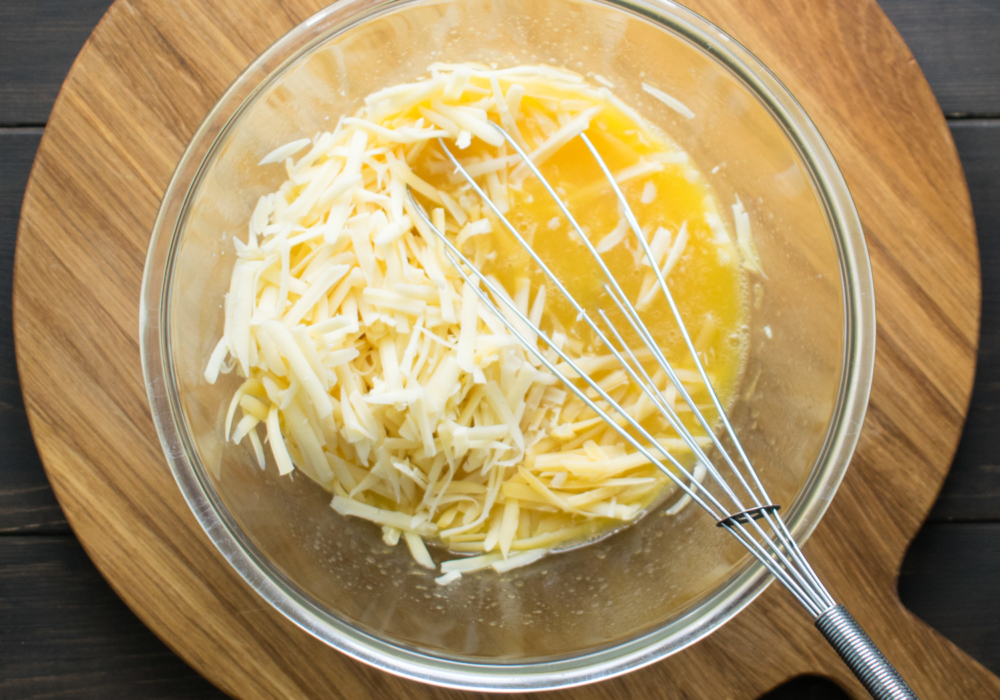 В миску к натертому сыру добавьте сырое яйцо.