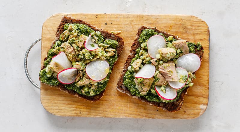 Тонко нарежьте редис. Намажьте все куски хлеба зеленой заправкой с одной стороны. Разложите тунец, накройте ломтиками редиса, поперчите. Подавайте сразу же.