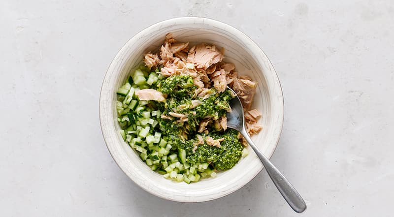 Слейте жидкость с тунца, она не понадобится. Мякоть разомните вилкой. Мелко нарежьте огурчик, соедините с тунцом, щедро поперчите и смешайте с ложкой зеленой заправки.