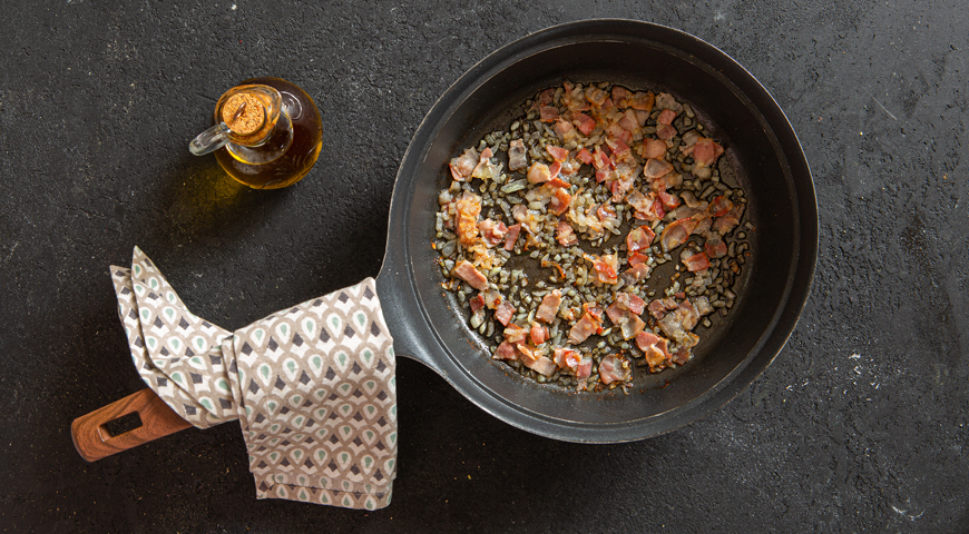 В сковородке с антипригарным покрытием разогрейте 2 ст. л. оливкового масла и выложите лук и бекон. Обжарьте на среднем огне до золотистого цвета, 5 мин.