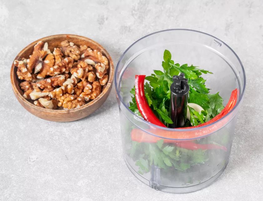 Сорвите с веточек петрушки листья и положите в чашу блендера. Туда же добавьте чеснок и чили. Положите сыр и орешки.