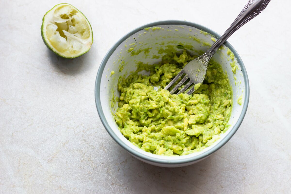 Авокадо делим на четыре части, удаляем косточку. Из кусков авокадо выбираем ложкой всю мякоть и разминаем ее вилкой так, чтобы оставались маленькие кусочки.