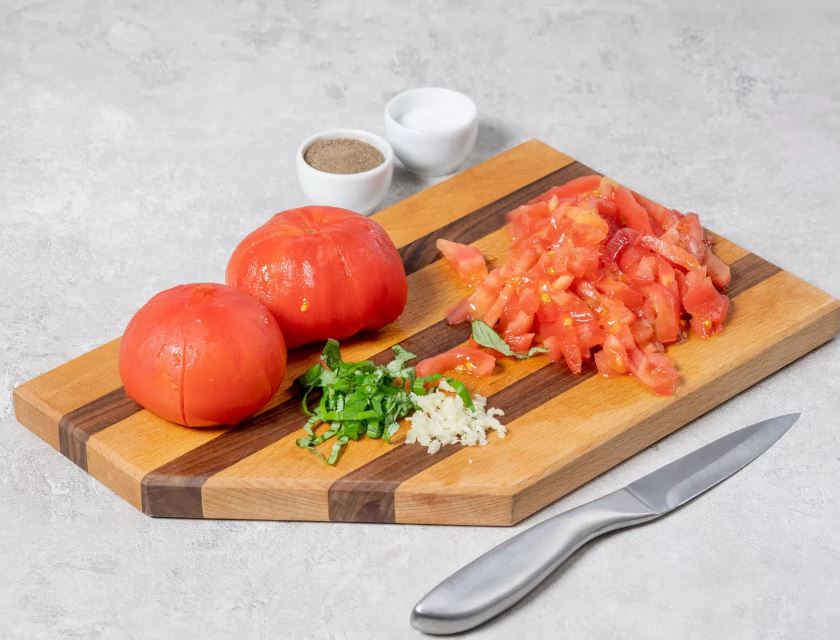 Ошпарьте помидоры кипятком и снимите с них кожицу. Нарежьте тонкой соломкой. Измельчите базилик и чеснок.