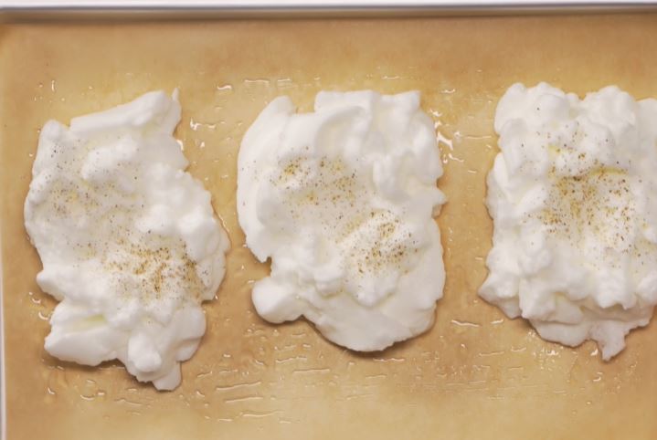 Взбитые белки выложить на противень, застеленный смазанной маслом бумагой, тремя одинаковыми порциями на расстоянии друг от друга. В центре каждой порции ложкой сделать небольшое углубление, по вкусу посолить и посыпать черным перцем.