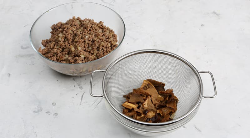 Мясной фарш с луком посолите и поперчите. Жарьте, периодически помешивая, около 10 минут на среднем огне. Переложите в отдельную емкость. Грибы откиньте на дуршлаг, промойте и мелко нарежьте.