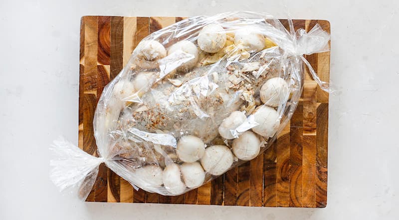 Захватите один край пакета клипсой. Выложите в пакет (на условное «дно», то есть чтобы сторона пакета, в которой есть крошечные отверстия, оказалась сверху) сначала слой картофеля, затем рыбу с грибами. Закрепите открытый край второй клипсой.