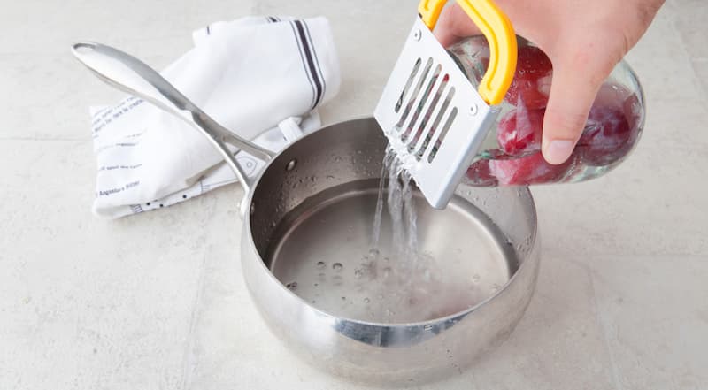 Слейте воду из банок в кастрюлю (для этого удобно воспользоваться специальной пластиковой крышкой с отверстиями). Добавьте сахар. Поставьте кастрюлю на огонь, доведите до кипения и проварите 3-4 мин. Сахар должен полностью раствориться.