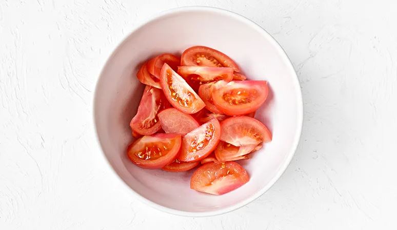 Подготовьте ингредиенты для греческого салата. Помидоры вымойте, затем хорошо обсушите. Удалите основания плодоножек, мякоть нарежьте дольками. Сложите в большую миску.