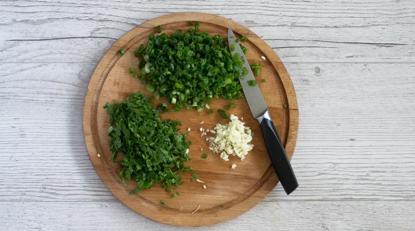 Зеленый лук для борща вымойте и нарежьте маленькими колечками. Чеснок очистите, раздавите плоской стороной ножа и порубите. Петрушку вымойте и очень мелко нарежьте.