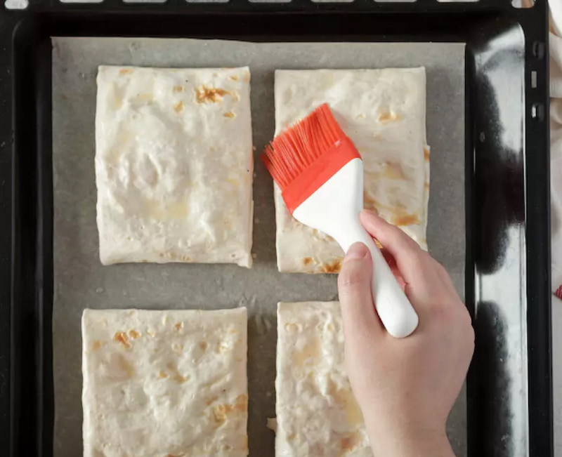 Подготовленные рулетики выложите на противень, застеленный пекарской бумагой, смажьте взбитым яйцом и посыпьте кунжутом. Выпекайте в предварительно разогретой до 200 °C духовке 15 минут.