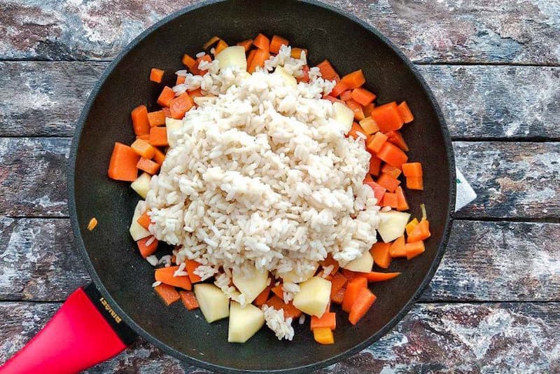 Всыпать рис к овощам. По вкусу добавить соль, молотый черный перец, итальянские травы. Жарить 2-3 минуты на умеренном огне помешивая.
