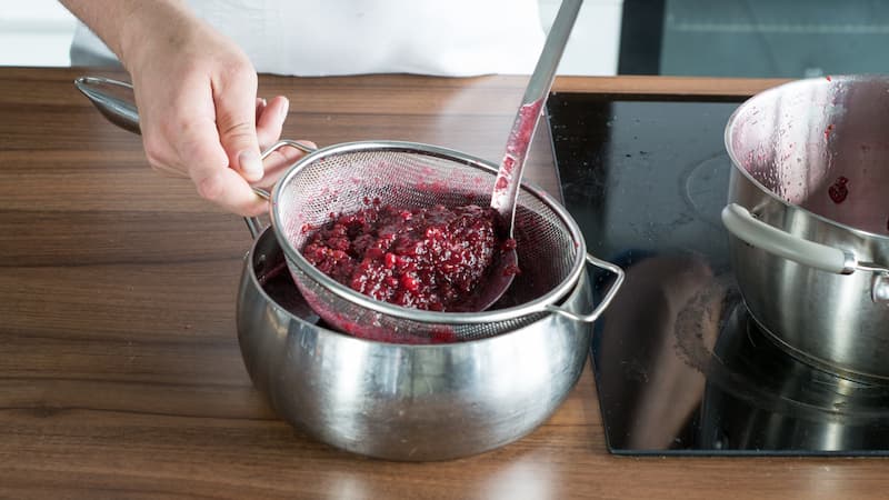 Содержимое кастрюли сразу же процедите через частое сито в большую миску или кастрюлю, не отжимая ягоды слишком сильно, иначе желе не получится прозрачным.
