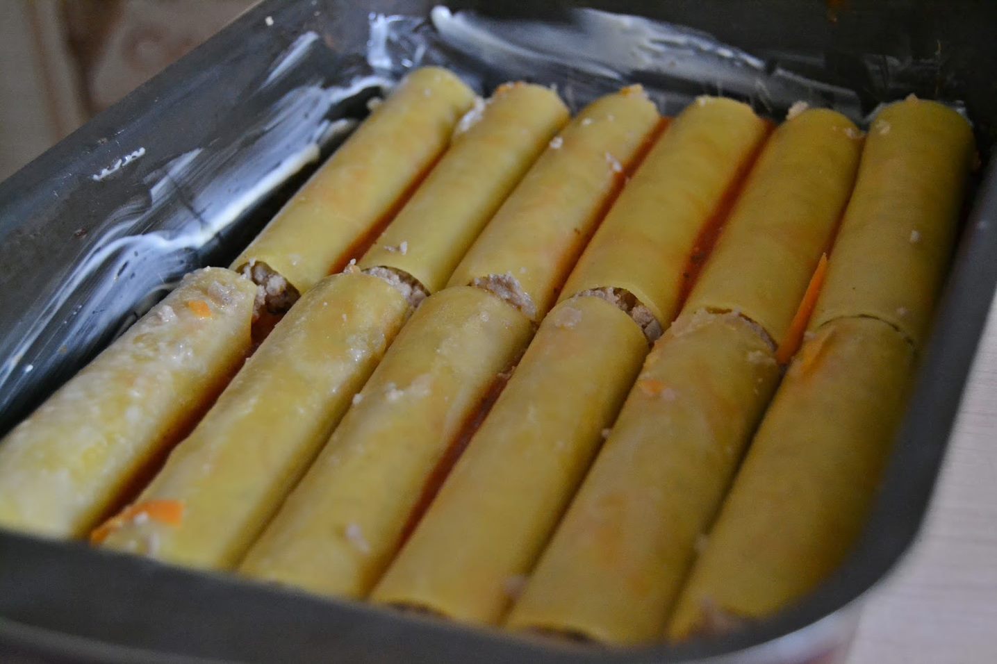 Форму смазать сливочным маслом и посыпать панировочными сухарями. Нафаршировать каннеллони фаршем.  Уложить нафаршированные каннеллони в форму плотно друг к другу. 