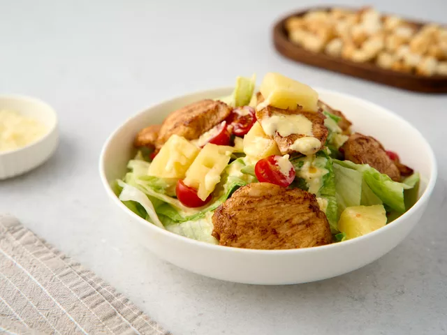 Разложите кусочки курицы, нарезанные пополам черри и ананас. Добавьте сухарики. Натрите 80 г пармезана и посыпьте салат.