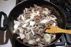 Лук чистим, нарезаем тонкой соломкой. Кидаем лук к мясу, перемешиваем, продолжаем жарить.