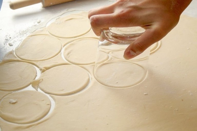 Из муки, яйца и воды замесить тесто, раскатать. Вырезать кружочки. На каждый кружочек положить картофель с луком, защипнуть края.