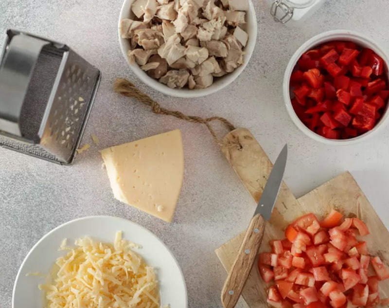 Филе куриного бедра предварительно отварите и нарежьте небольшими кусочками. Перец очистите от семян и нарежьте кубиками. Так же нарежьте помидоры. Сыр натрите на крупной терке.