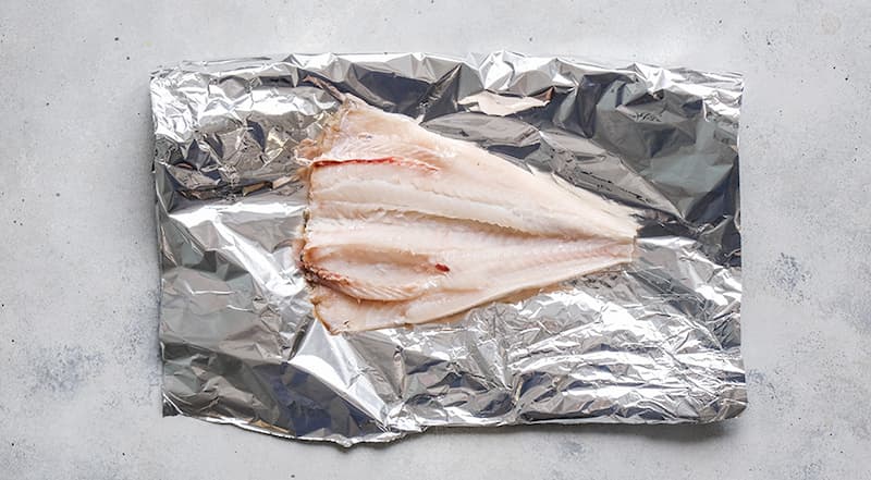 Подготовьте все ингредиенты. Треске дайте полностью оттаять на самой «теплой» полке холодильника. Затем вымойте рыбу, отрежьте голову, брюшко выпотрошите. Плавники и хвост отрежьте. Разрежьте пополам и поместите на большой лист фольги.