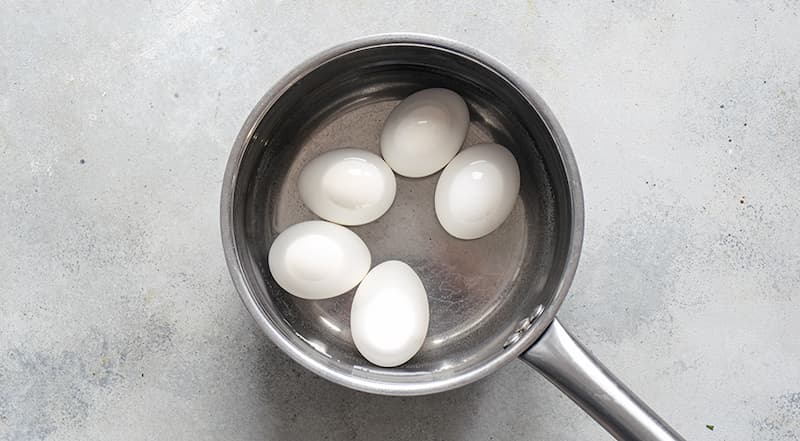 Подготовьте все ингредиенты закуски. Яйца вымойте и поместите в ковшик. Залейте холодной водой и доведите до кипения. Варите на среднем огне 10 минут, затем охладите проточной водой.