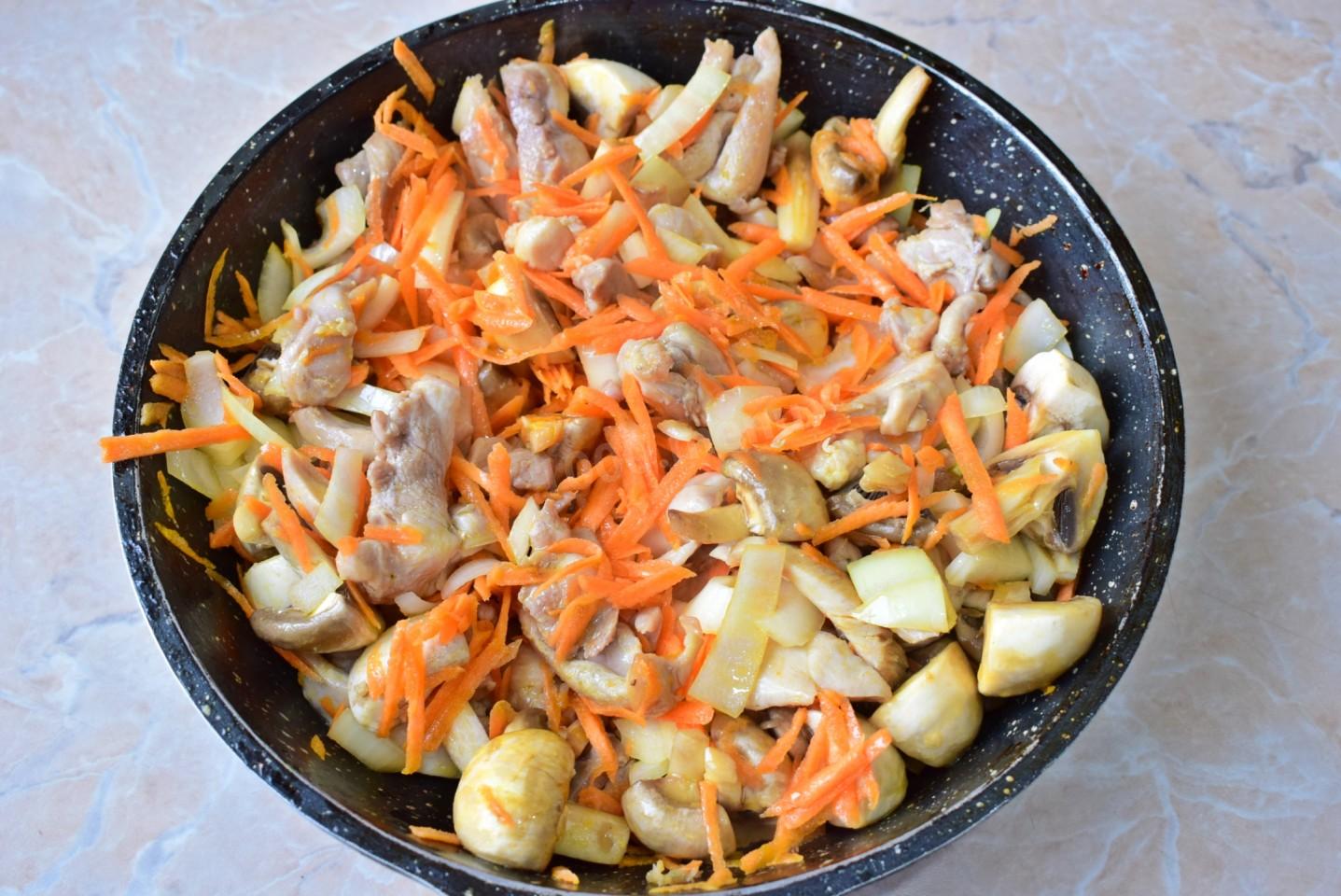В сковороде с толстым дном разогрейте растительное масло. Отправьте курицу, морковку, лук и шампиньоны в сковороду. Обжарьте мясо, овощи и грибы, постоянно помешивая, около 5-7 минут. 