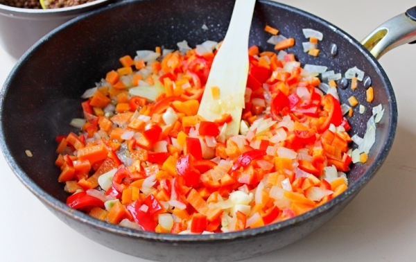 Лук, морковь и перцы измельчите мелкими квадратиками. Разогрейте рафинированное растительное масло в сковороде. Отправьте лук, морковь и болгарские перцы обжариваться. Если вы используете перец чили, то добавьте его тоже. Готовьте на сильном огне, помешив