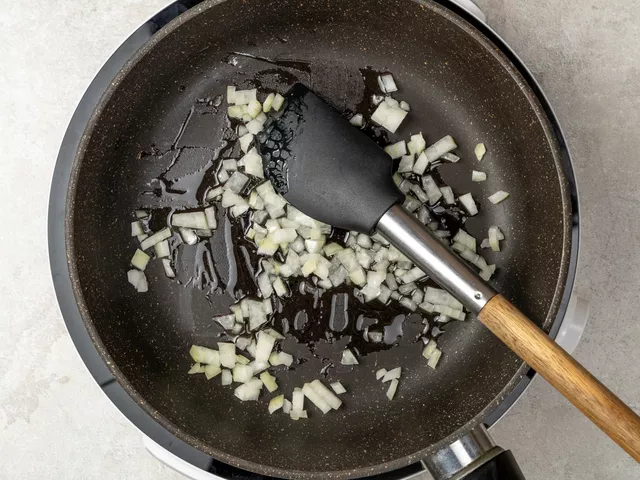 Нарежьте репчатый лук мелкими кубиками. Переложите в сковороду и обжарьте, помешивая, в течение 5-7 минут.