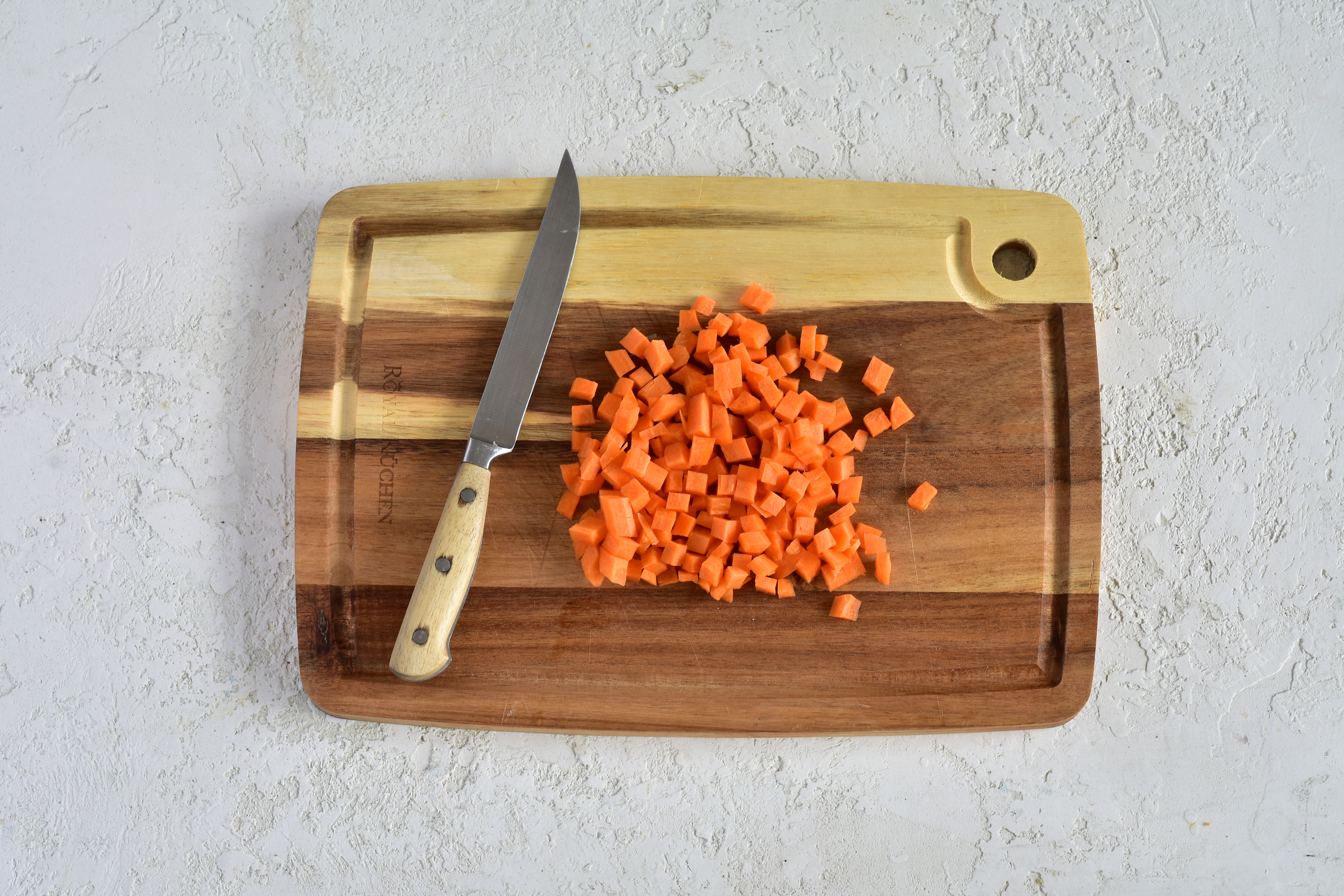 Морковь вымойте при помощи овощной щеточки, очистите от кожуры, а затем тоже нарежьте маленькими кубиками такого же размера, что и кабачок.