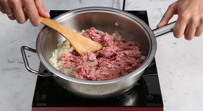 Луковицу очистите и мелко порубите. В сковороду, где тушилась капуста, влейте 1 ст. л. растительного масла и нагрейте его. Положите лук и слегка подрумяньте. Добавьте фарш и, помешивая, жарьте до изменения цвета.