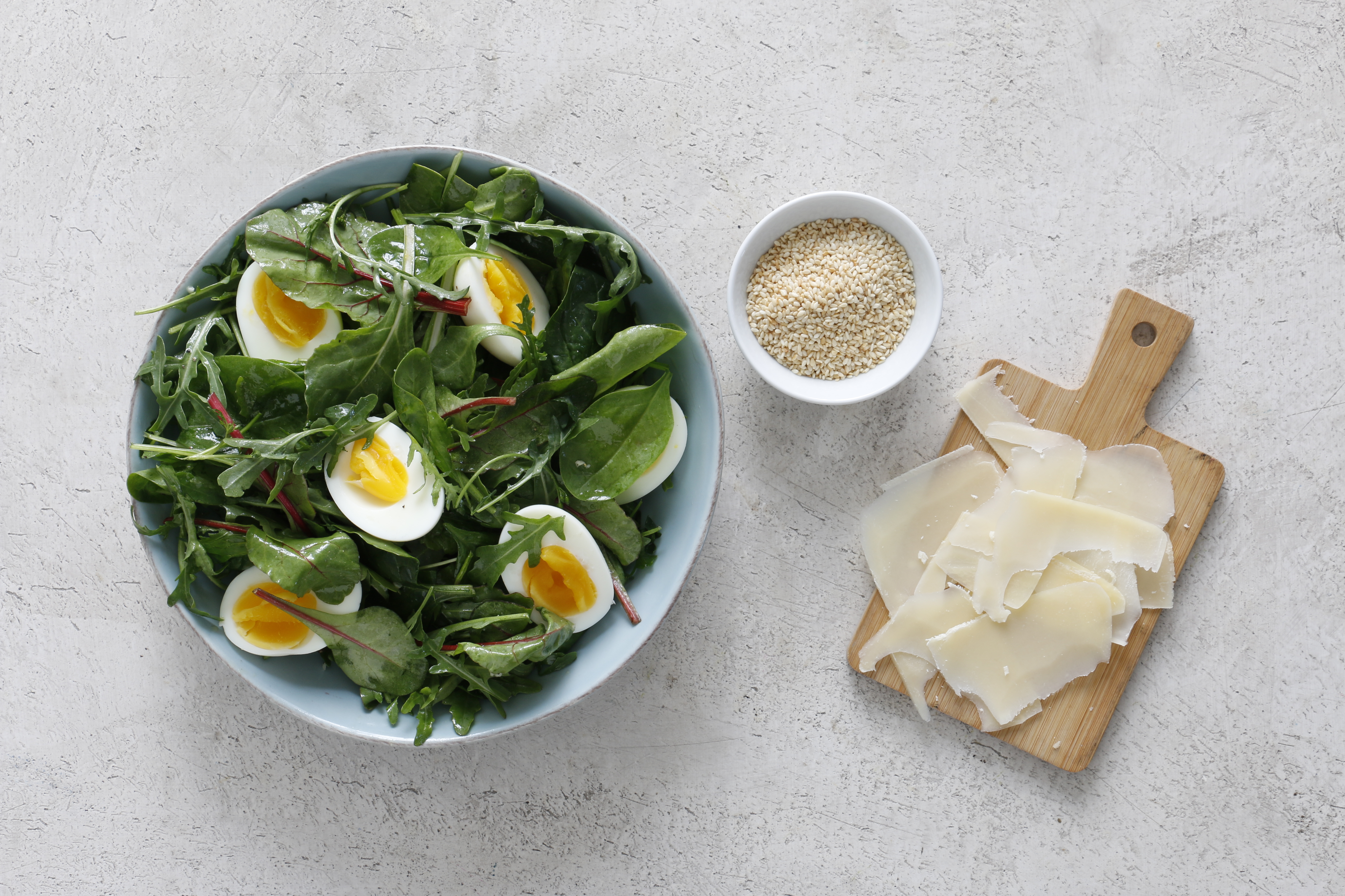 Салатные листья смешайте с заправкой и разложите на тарелки. Сверху положите по две половинки яйца. Посыпьте стружкой твердого сыра. (ее удобно делать ножом для чистки овощей). Украсьте жареным кунжутом.