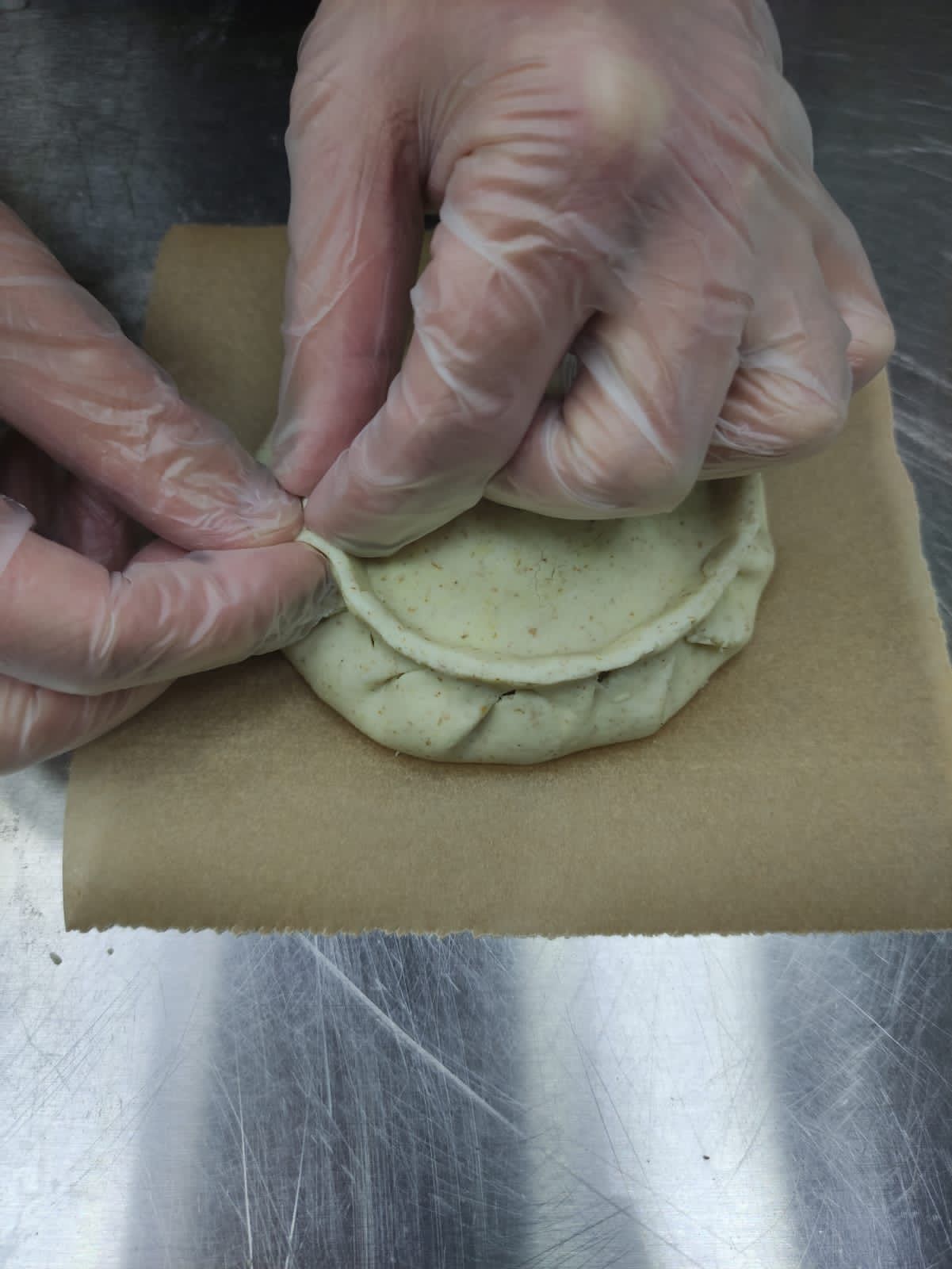 Поверх начинки положить маленький кружок теста. Поднять края нижнего круга и начать защипывать с крышечкой