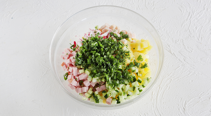 Зеленый лук и укроп для окрошки вымойте и обсушите бумажными полотенцами. Мелко нарежьте, затем сложите в большую миску. Добавьте редис, свежие огурцы, картофель, вареную ветчину, колбасу и яйца.